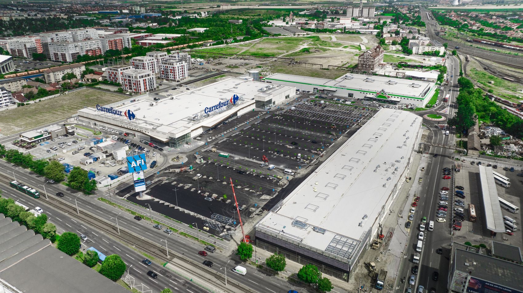 Vedere aeriană a parcului comercial AFI Arad, cu clădirile comerciale, o parcare nouă în lucru și o macara pe șantier
