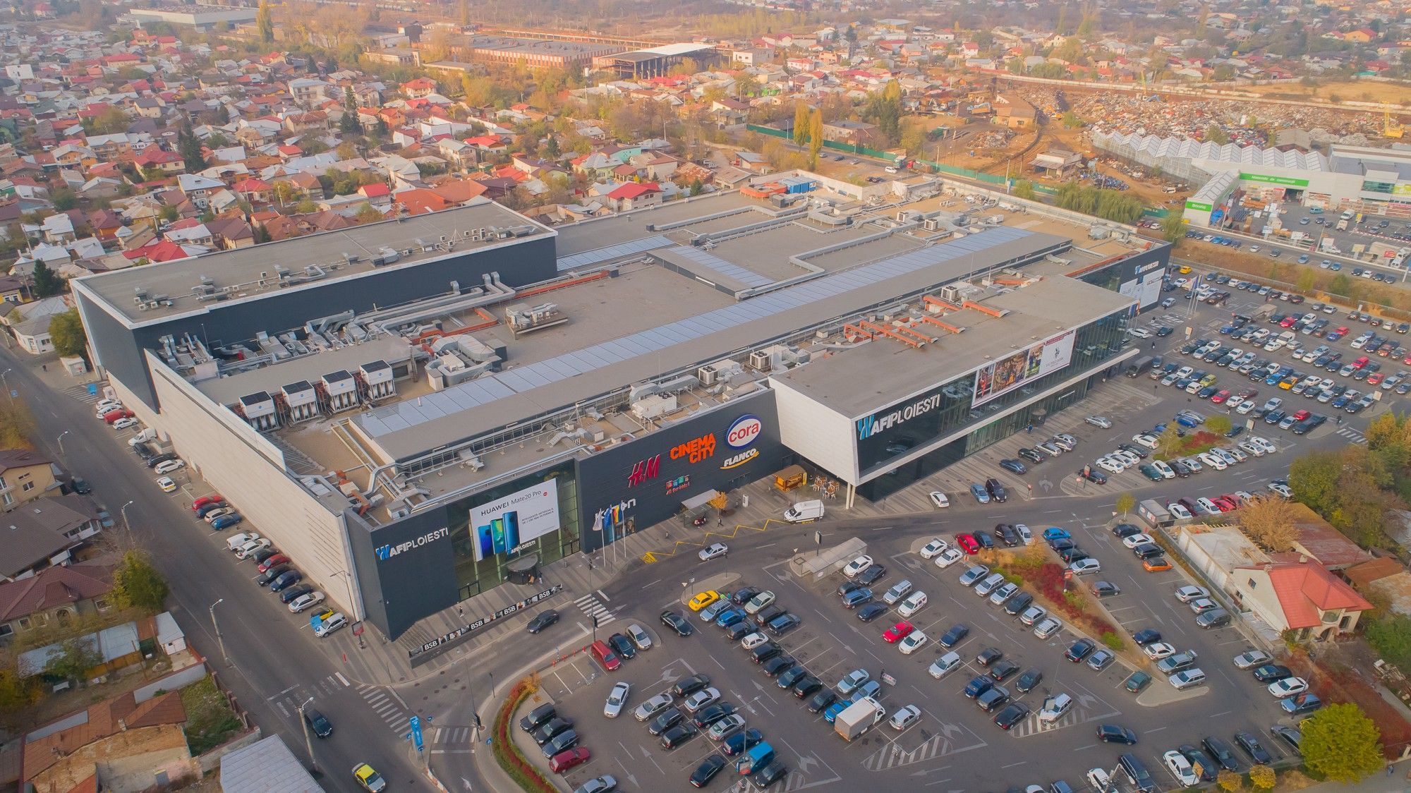 Vedere aeriană a centrului comercial AFI Palace Ploiești, cu parcarea plină de mașini și cartierul de case din jur