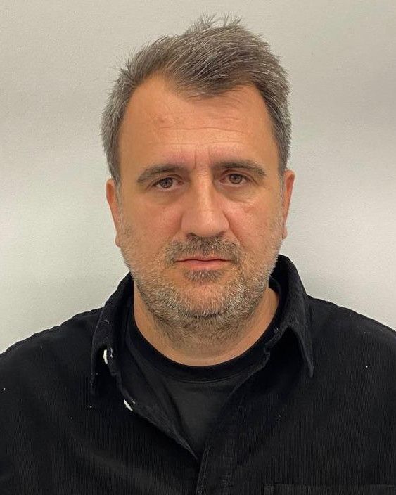 Portretul lui Bogdan Calistrata, în cămașă neagră peste un tricou negru, pe un fundal gri deschis